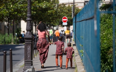 Une femme noire tient par la main ses deux enfants. Ils se promènent dans la rue à Paris.