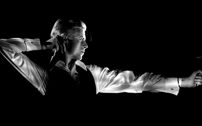 Portrait en noir et blanc de David Bowie, photographié de profil comme s'il tirait à l'arc