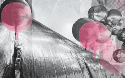 Sur cette image en noir et blanc, une structure gonflable est visible, réalisée à partir de couvertures de survie, avec une texture brillante et plissée.  Autour de cette structure, plusieurs ballons ronds de couleur rose sont dispersés, certains semblant sortir de l'intérieur de la structure, flottant autour d'elle.