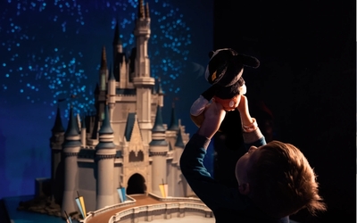 Enfant de dos, tenant une peluche mickey devant la maquette du chapeau Disney