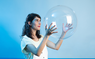 Une femme brune, sur un fond bleu ciel, tient une bulle transparente dans ses mains 